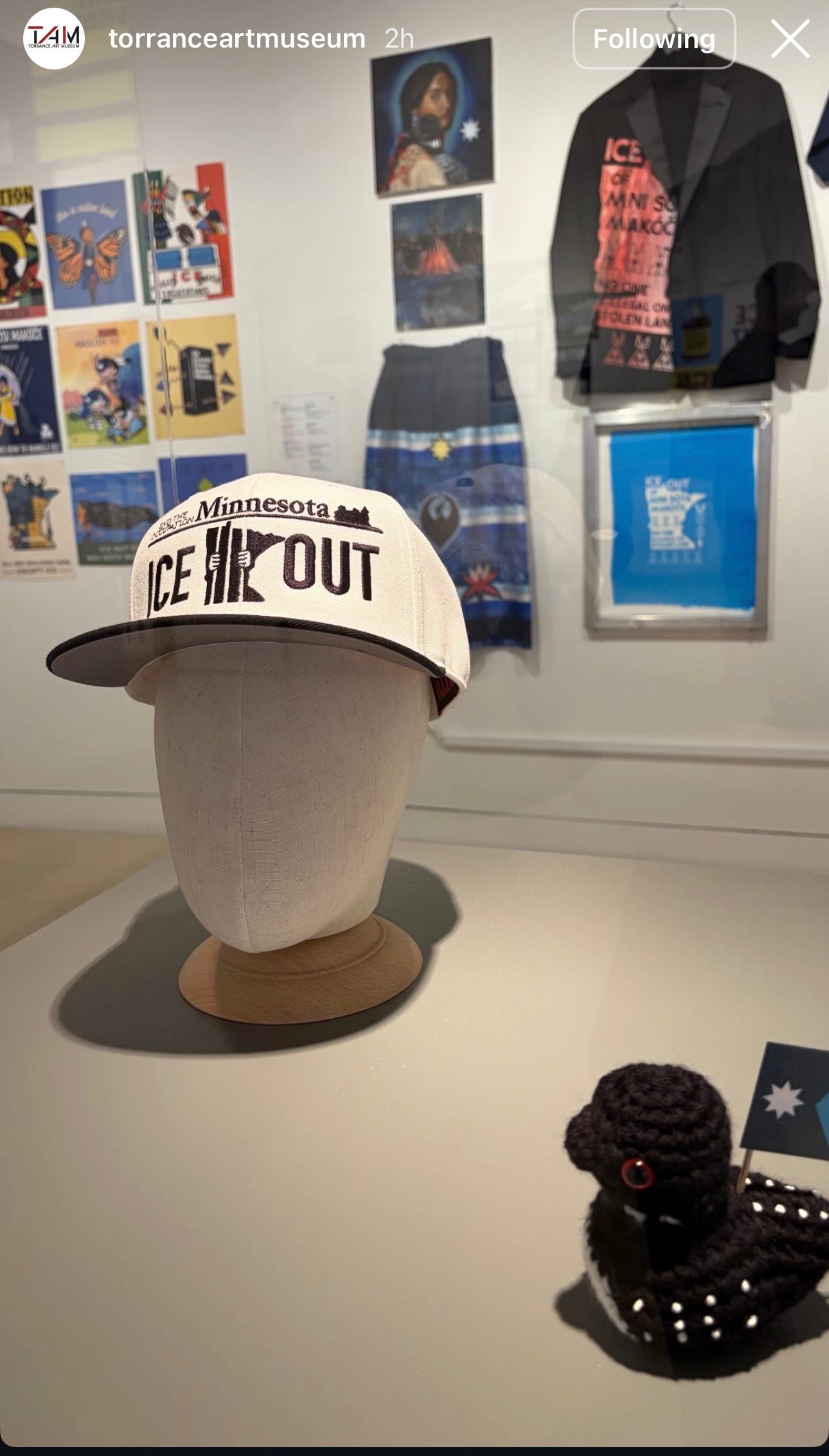 Cap with 'Ice Out' text on a mannequin head in an art museum setting.