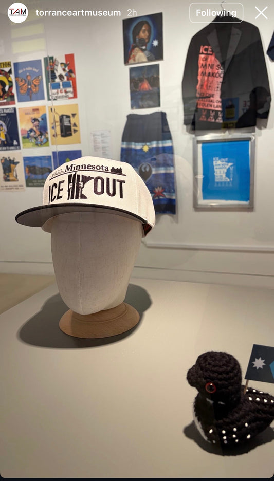 Cap with 'Ice Out' text on a mannequin head in an art museum setting.
